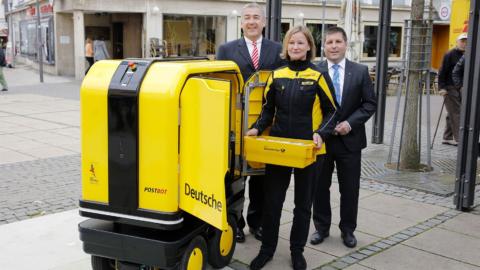 De izquierda a derecha, Jürgen Gerdes, CEO de la división Post –eCommerce- Parcel en DHL, una trabajadora de Deutsche Post probando el PostBOT y Thomas Fehling, alcalde de Bad Hersfeld.